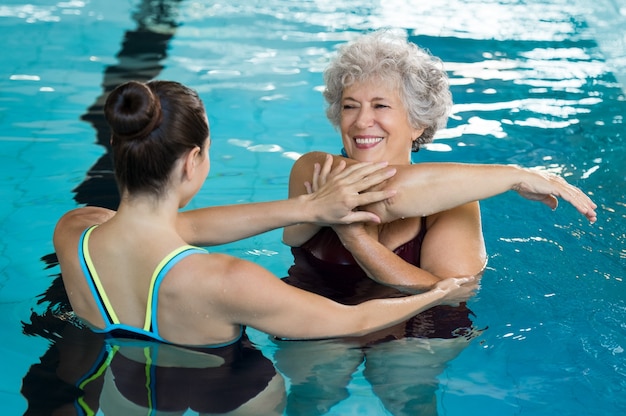 Young trainer helping senior woman in aqua aerobics