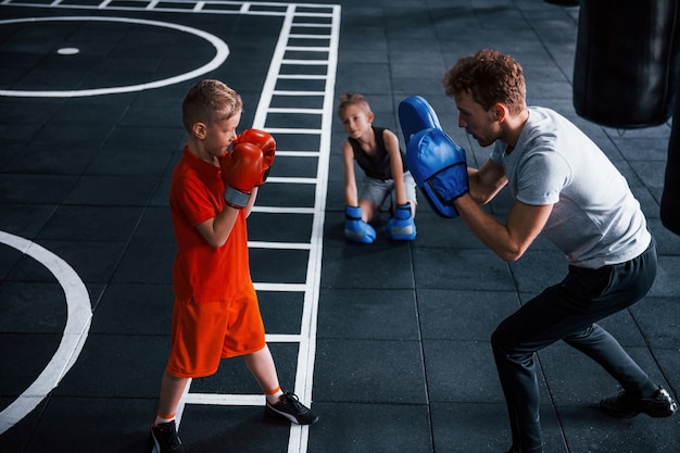 젊은 트레이너는 체육관에서 아이들에게 권투 스포츠를 가르칩니다.