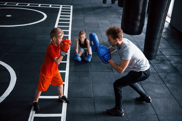 Young trainer teaches kids boxing sport in the gym.