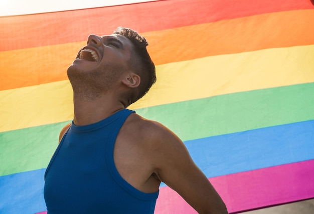 Giovane uomo transgender con il trucco che sorride con la bandiera arcobaleno lgbt sullo sfondo