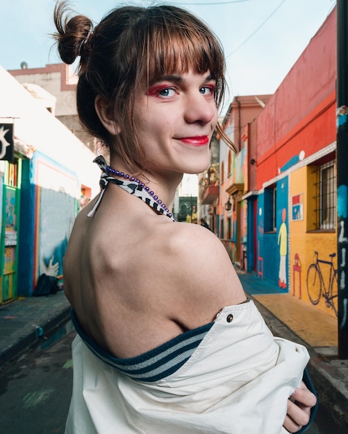 Young transgender woman on the street standing sideways with a jacket half on looking at the camera