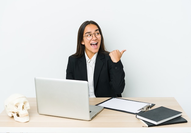 Young traumatologist asian woman isolated on white points with thumb finger away, laughing and carefree.