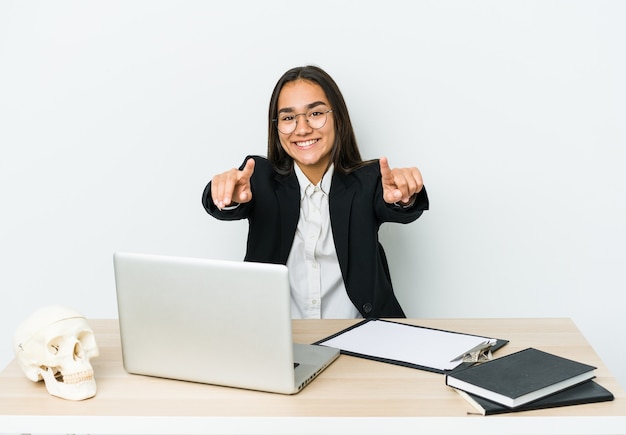 Young traumatologist asian woman isolated on white wall cheerful smiles pointing to front.