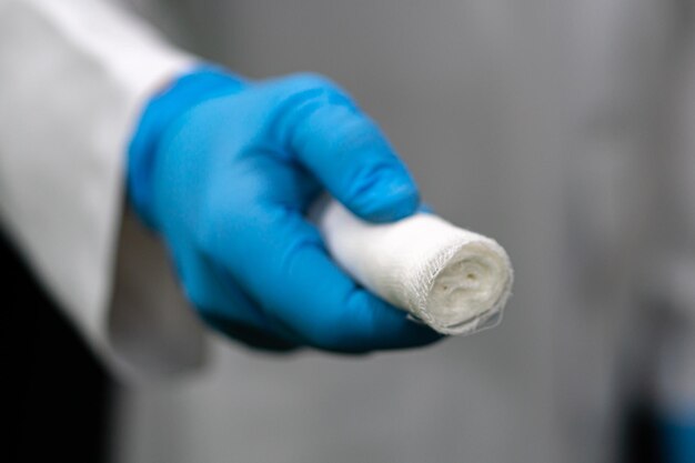 A young traumatologist holds a white medical bandage in his hand A doctor in a white coat and a bandage in his hands on a black background