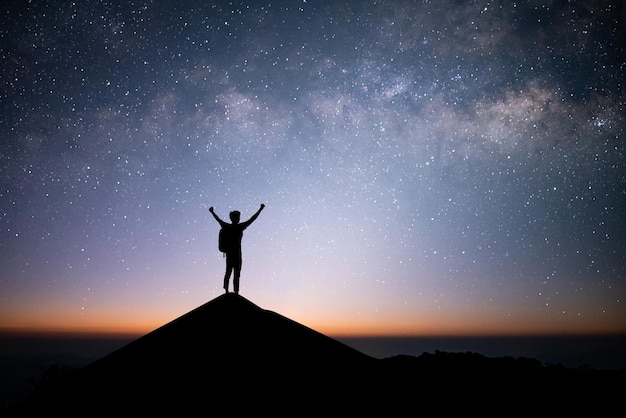 Young traveler and backpacker standing and open arm watched the\
star and milky way alone on top of the mountain he enjoyed\
traveling and was successful when he reached the summit