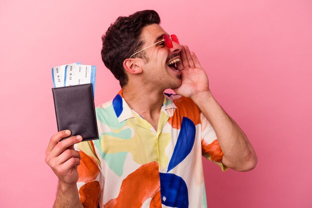 Young traveler caucasian man holding a passport isolated on pink background shouting and holding palm near opened mouth.