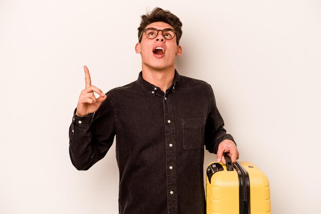 Young traveler caucasian man holding a suitcase isolated on white background pointing upside with opened mouth