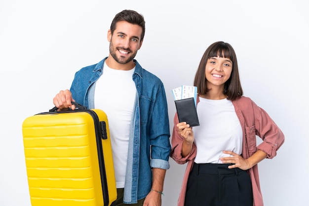 Young traveler couple holding a suitcase and passport isolated on white background posing with arms at hip and smiling