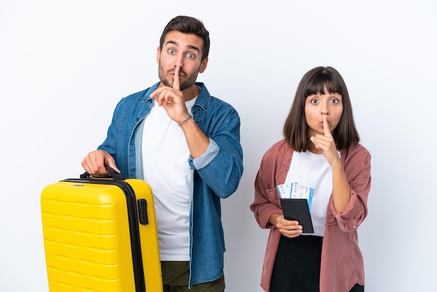 흰색 배경에 격리된 가방과 여권을 들고 있는 젊은 여행자 부부는 입에 손가락을 넣는 침묵 제스처의 표시를 보여줍니다.