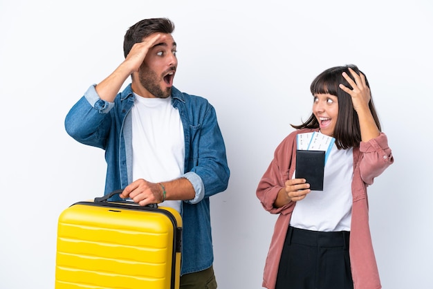 Coppia di giovani viaggiatori in possesso di una valigia e passaporto isolati su sfondo bianco con espressione facciale sorpresa e scioccata