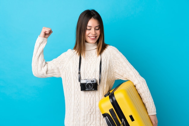 Ragazza giovane viaggiatore con la valigia sul muro blu