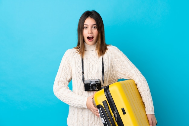 青い壁の上のスーツケースを持つ若い旅行者の女の子