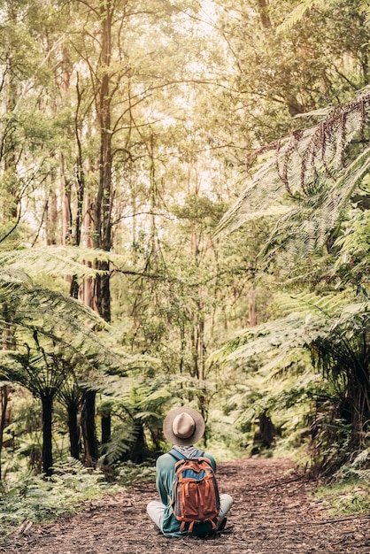 Young traveler lost in the forest with a hat sits and meditates on the ground during sunset