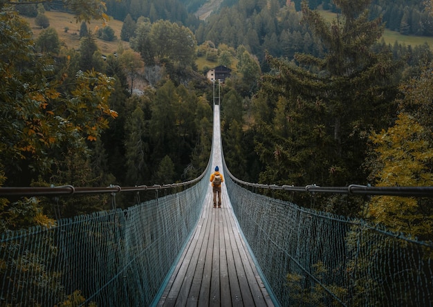 Young traveler man dressed in yellow jacket crosses hiking on an impressive wooden and metal bridge