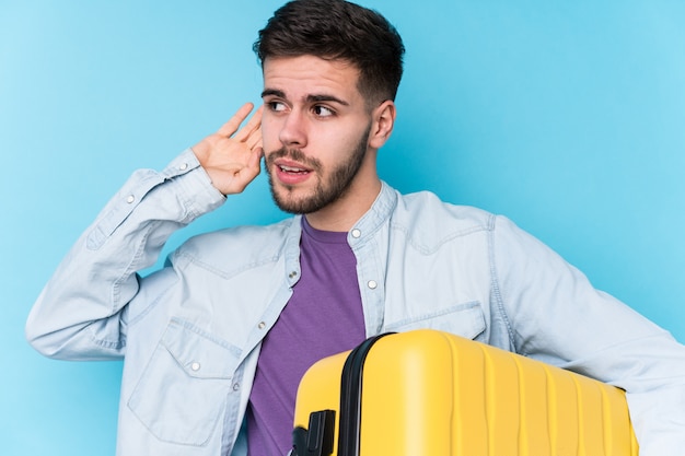 Young traveler man holding a suitcase isolated trying to listening a gossip