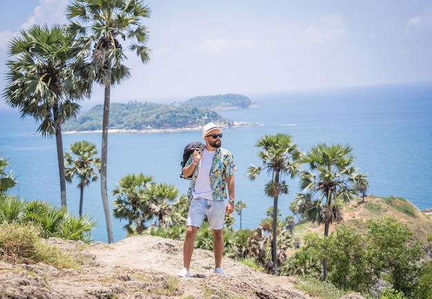 背景に美しい山々と海の風景と夏休みの若い旅行者の男