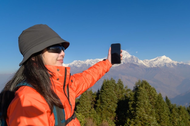 A young traveler takes a selfie or a video call while standing a top a mountain