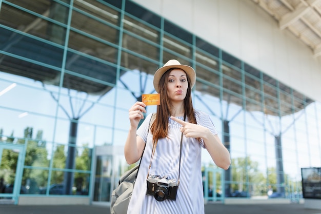 Giovane donna turistica viaggiatrice in cappello con macchina fotografica vintage retrò, puntando il dito indice sulla carta di credito all'aeroporto internazionale