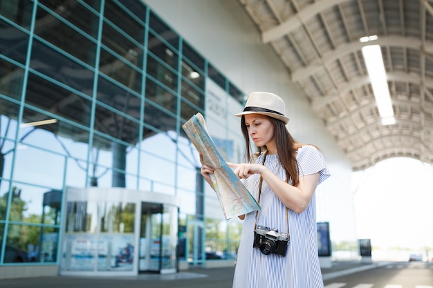 国際空港の紙の地図でレトロなビンテージ写真カメラ検索ルートを持つ若い旅行者観光客の女性