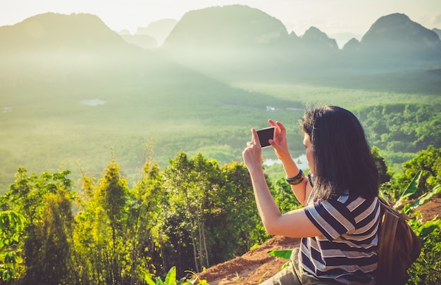 若い旅行者の女性のバックパッカー携帯電話を使用して山の頂上で日の出の美しい写真を撮る