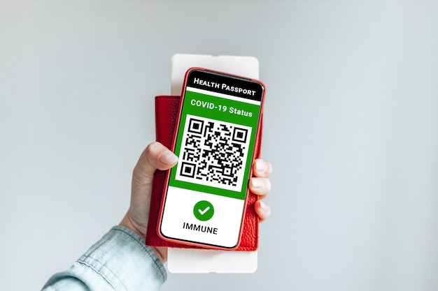 Young traveler woman hand shows health passport of vaccination certification on phone at airport or train platform, to certify that have been vaccinated of coronavirus covid-19