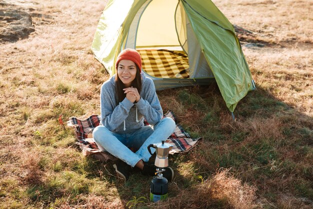 テントの近くで朝屋外に座っている若い旅行者の女性