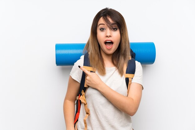 Young traveler woman over white wall surprised and pointing side