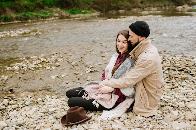 若い旅行者のカップルは、背景の山川でお互いを抱きしめます