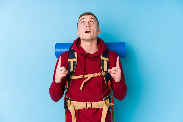 Young traveller caucasian man pointing upside with opened mouth.