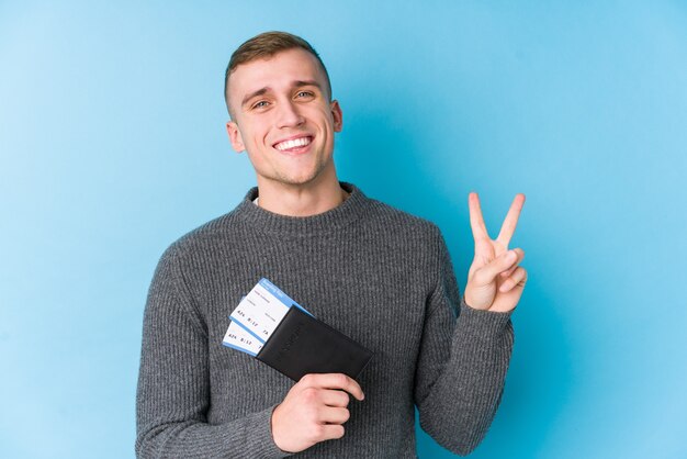 Young traveller man holding a boarding pass joyful and carefree showing a peace symbol with fingers.