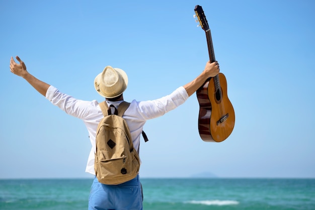 young traveller man lift guitar on the beach with freedom.