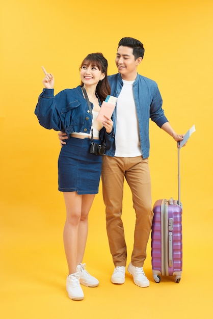 Young travelling couple with suitcases pointing somewhere isolated on yellow