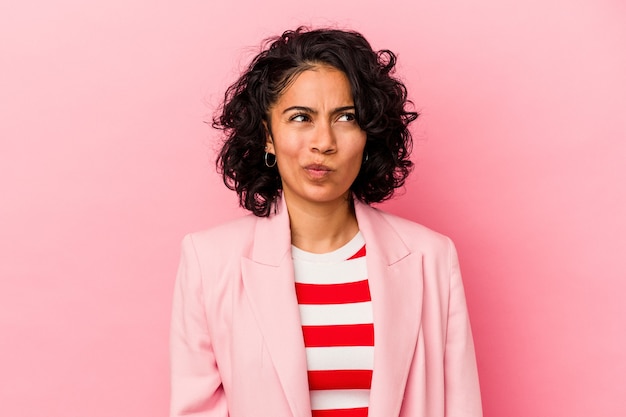 Young trendy latin woman isolated on pink background confused, feels doubtful and unsure.