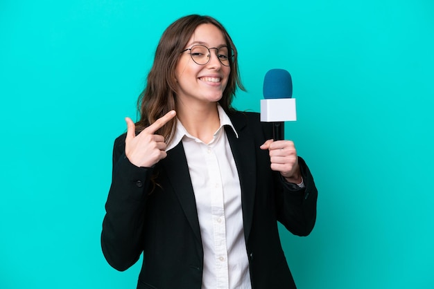 Young TV presenter woman isolated on blue background giving a thumbs up gesture