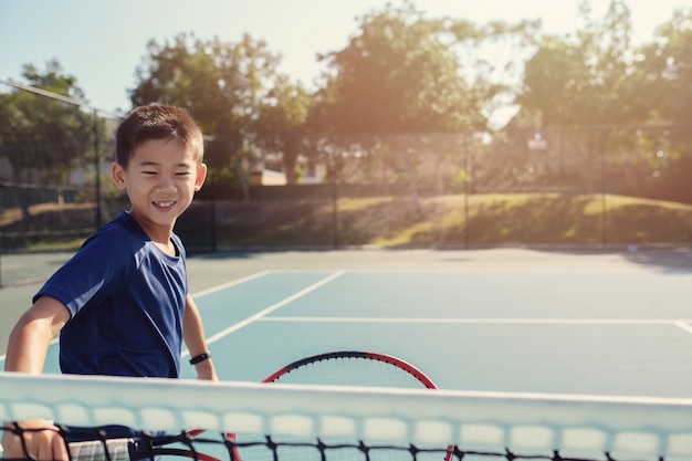 Young tween Asian boy tennis player on outdoor blue court