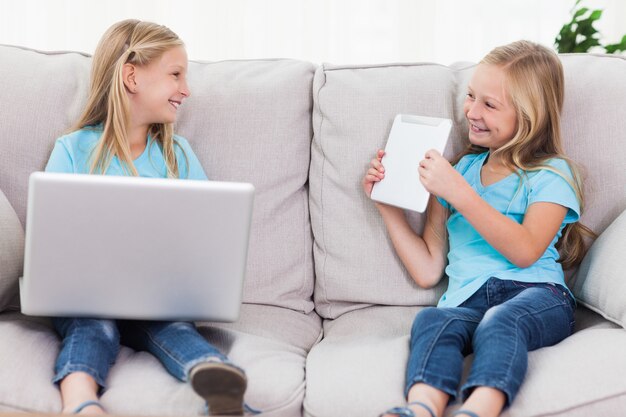 Молодые близнецы, используя ноутбук и планшет, сидя на диване