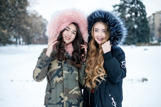 Young two woman winter portrait. Shallow dof. Beautiful smiling face of fashion model with red lips and fur hood