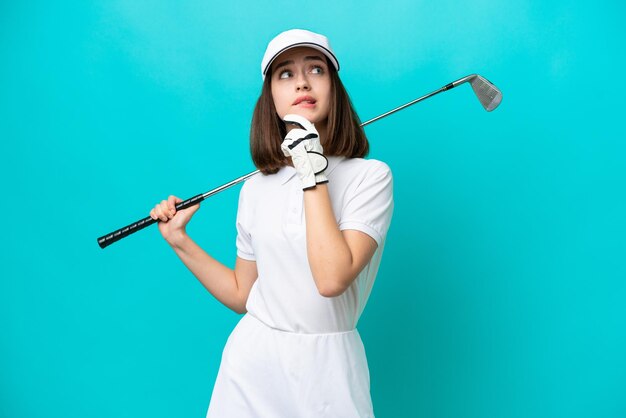 Young Ukrainian golfer player woman isolated on blue background having doubts and thinking