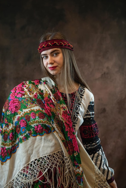 Young Ukrainian lady in an embroidered blouse and a shawl poses against a dark background National clothes ethnic and folklore