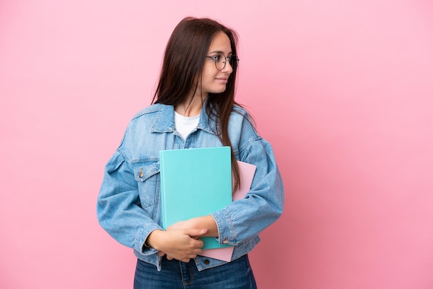 Young Ukrainian student woman isolated on pink background looking to the side