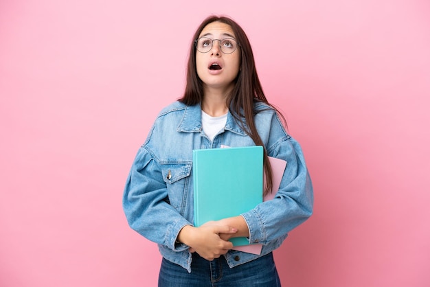 Young Ukrainian student woman isolated on pink background looking up and with surprised expression