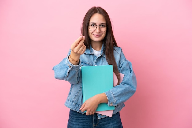 Young Ukrainian student woman isolated on pink background making money gesture