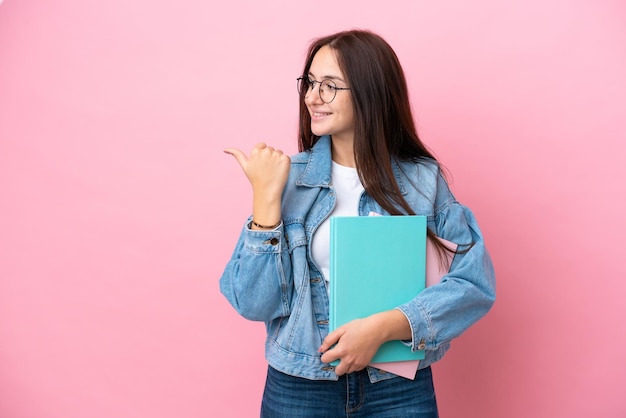 製品を提示する側を指しているピンクの背景に分離された若いウクライナの学生女性