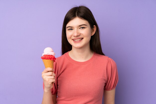 Giovane ragazza ucraina dell'adolescente che tiene un gelato della cornetta sopra la parete porpora isolata che sorride molto