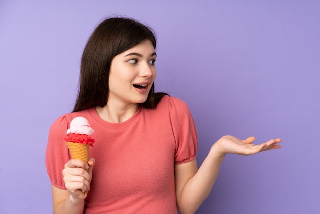 Young Ukrainian teenager girl holding a cornet ice cream over purple wall with surprise facial expression