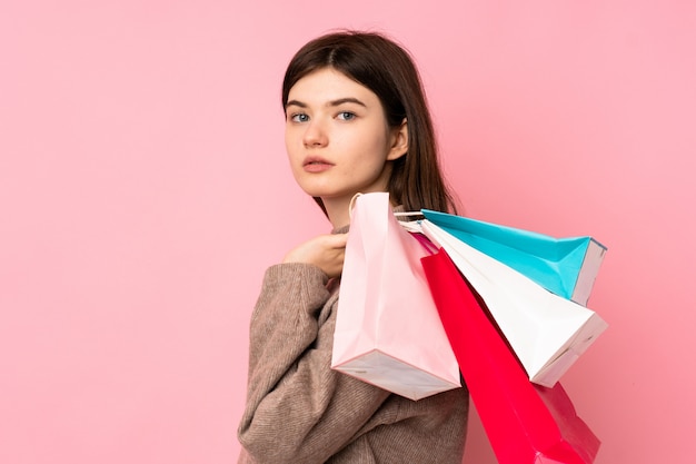 Young Ukrainian teenager girl over isolated pink wall holding shopping bags