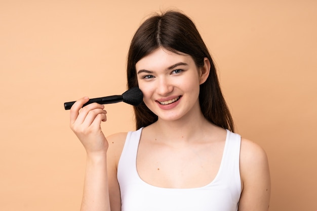 Young Ukrainian teenager girl over wall holding makeup brush and whit happy expression