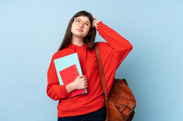 Young Ukrainian teenager student woman holding a salad over isolated blue wall having doubts and with confuse face expression