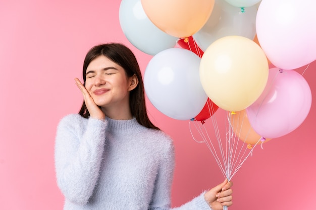 Young Ukrainian teenager woman holding lots of balloons over isolated pink wall