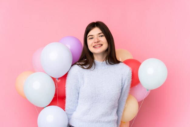 Young Ukrainian teenager woman holding lots of balloons over isolated pink wall